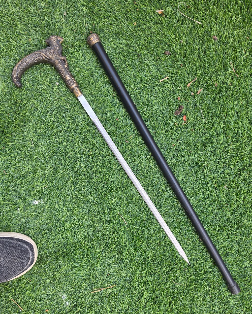 מקל הליכה משולב עם חרב נסתרת (Sword Cane), הכולל ידית מתכת מעוטרת ברוב הדורים ונדן שחור 