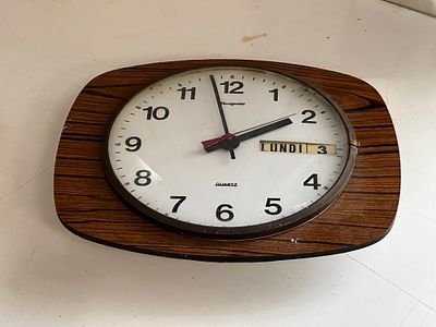 שעון קיר וינטג’ Hegner עם מנגנון קוורץ ותצוגת יום ותאריך. דגם בעיצוב אופייני לשנות ה־70–80, עם 