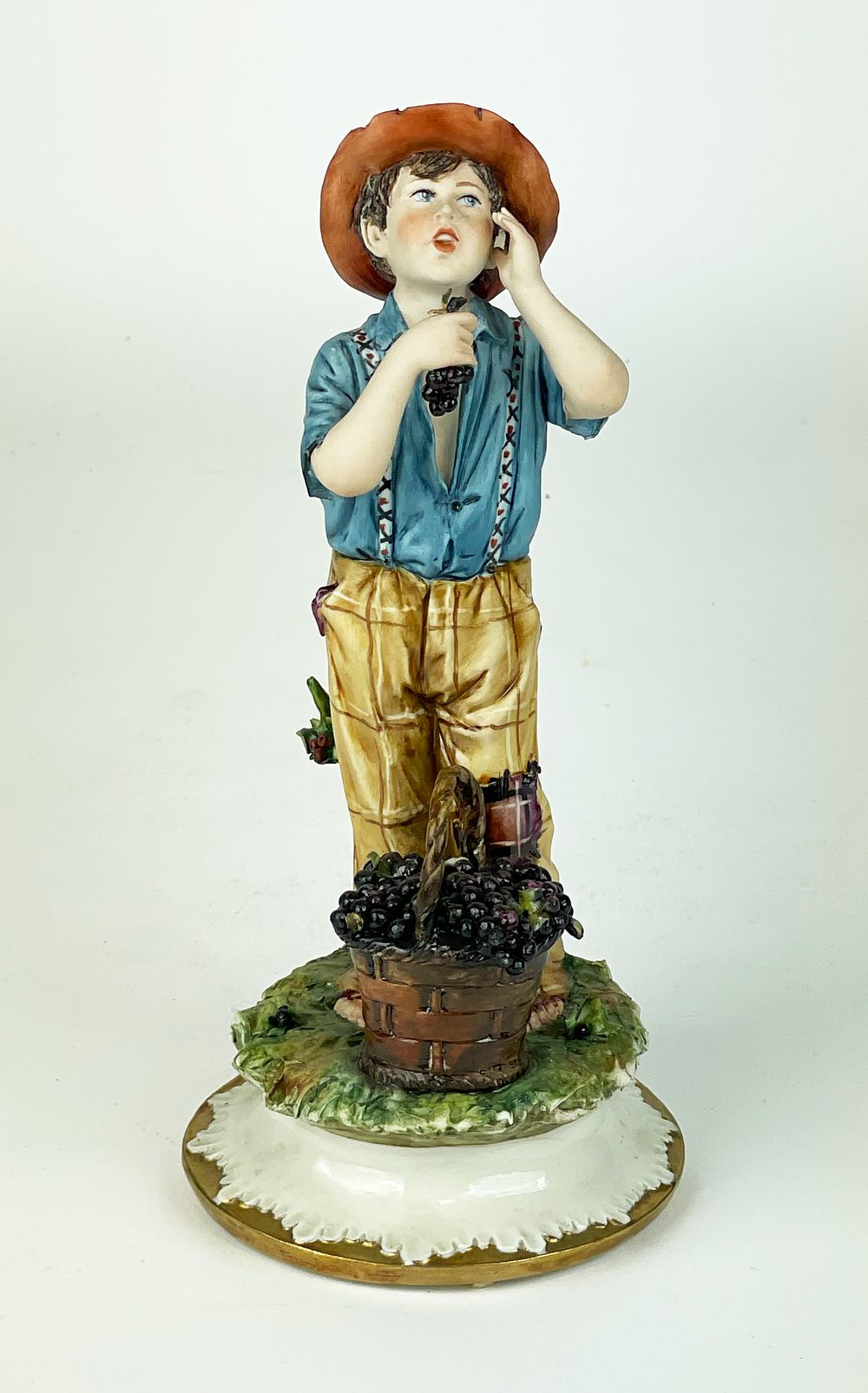 Polychrome artistic porcelain, marked Capodimonte, depicting a standing boy with a fruit in his 