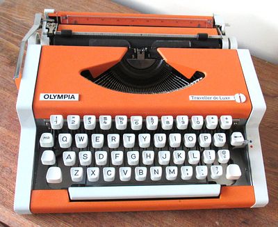 OLYMPIA TRAVELLER DE LUXE TYPEWRITER. SOUGHT AFTER ORANGE. EXC. CONDITION. APPEARS UNUSED.