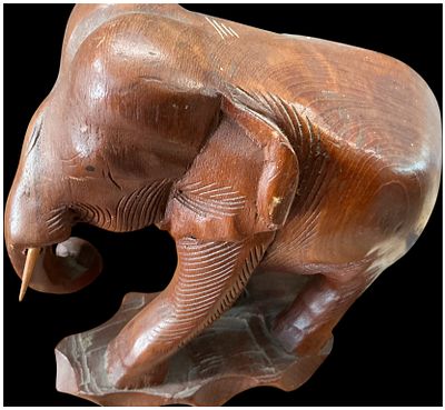 Large Hand Carved Teak Elephant Figure. A hand-carved teak wood figure of an elephant, depicted 