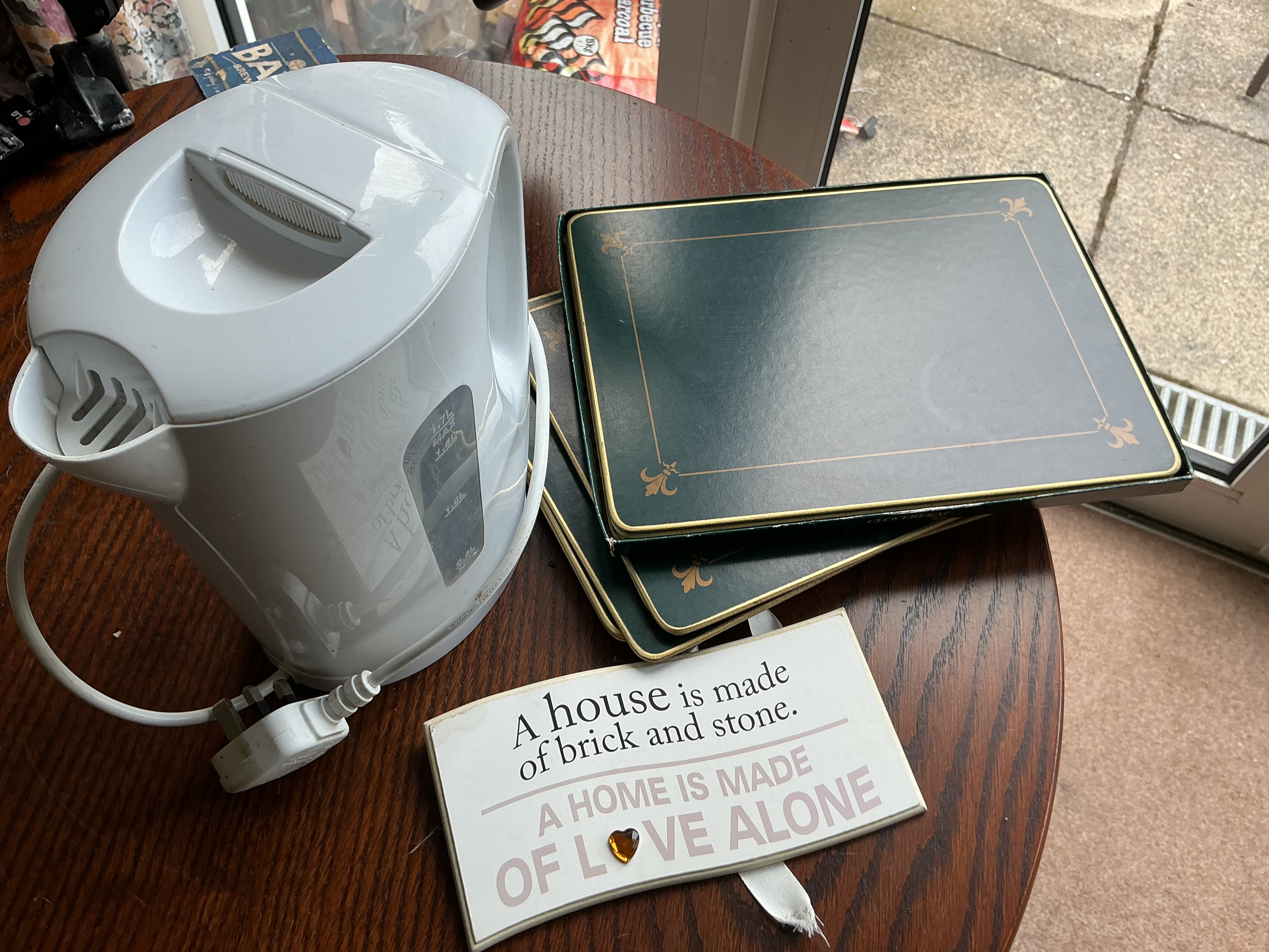 An assortment of domestic items including an electric kettle, Cloverleaf placemats, and a decorative plaque