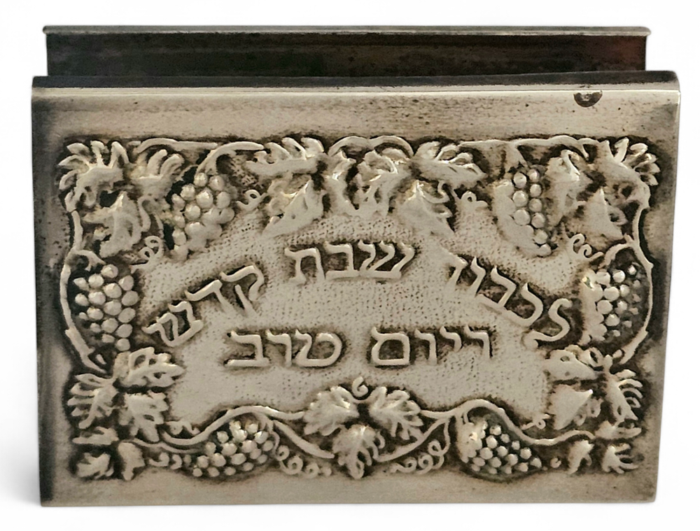 מחזיק גפרורים עשוי כסף סטרלינג, עם מוטיב עלי גפן ואשכולות ענבים, והמילים "לכבוד שבת קודש ויום 