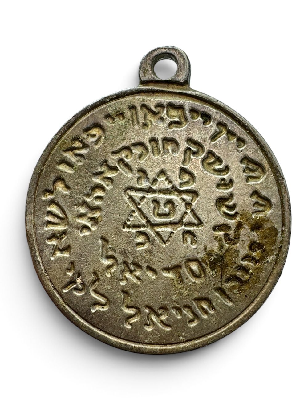 קמע תליון קבלי, להגנה ושמירה. היה שייך לרב ושוחט מרמת גן שהלך לעולמו בטרם עת. מידות: 4.3x5 ס״מ.