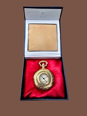 שעון כיס (Pocket Watch) בעל עיצוב וינטג' קלאסי בצבע זהב, המונח בקופסת תצוגה מרופדת בבד קטיפה אדום.