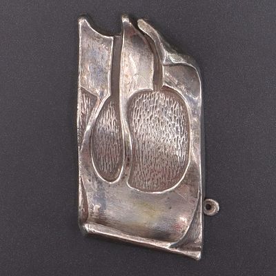 מזוזת כסף חתומה "Bruria", עבודת יד כיפוף ובלט דוגמת האות "ש" בצורת מגילה. . 9.5X5 ס"מ, משקל 51 גרם.