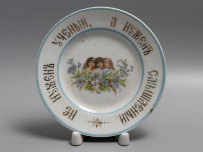 Тарелка &laquo;Не нужен ученый, а нужен смышленый&raquo;. Фарфор. Нач. XX в. Диаметр 15 см. 
Тонкие трещины 