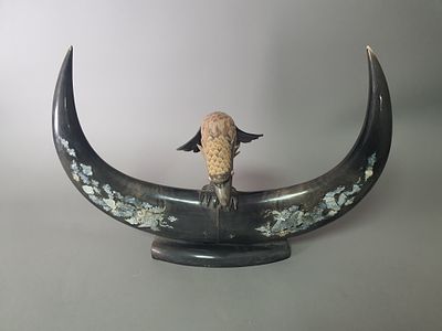 פסלון מרהיב של ציפור דורסת על שתי קרניים משובץ בעבודת צדף. הכל עשוי קרן בצבעים שונים. המזרח הרחוק.