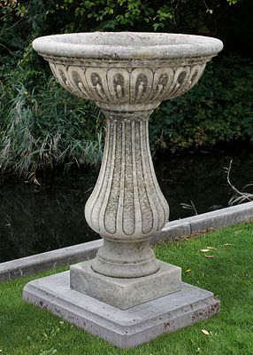 A CARVED LIMESTONE PLANTER ON A PLINTH. The vase, in a Roman or neoclassical style, has a 