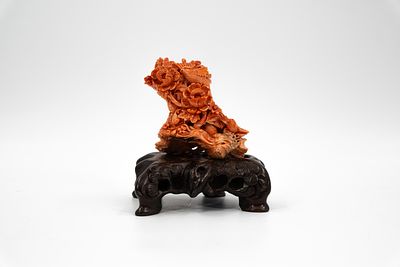 A Chinese carved red coral sculpture decorated with animals and flowers, on a carved wood base. 