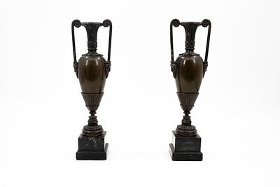An antique pair of patinated bronze vases with handles and crowned male heads. Footed on black 