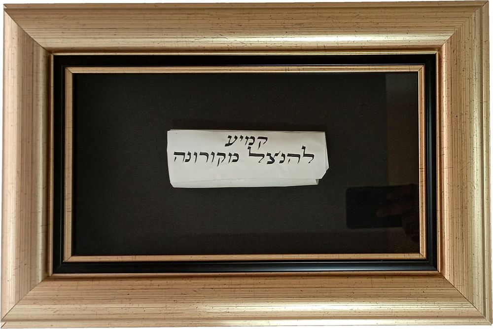 קמיע להנצל מקורונה - נתון במסגרת לתלייה . קמע עם שמות קודש כתוב בדיו על קלף לשמירה מפני מגפת