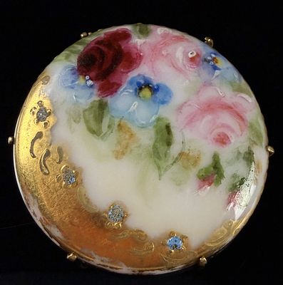 Hand-Painted Porcelain Floral Brooch with Gilded Scrollwork. This circular brooch features a 