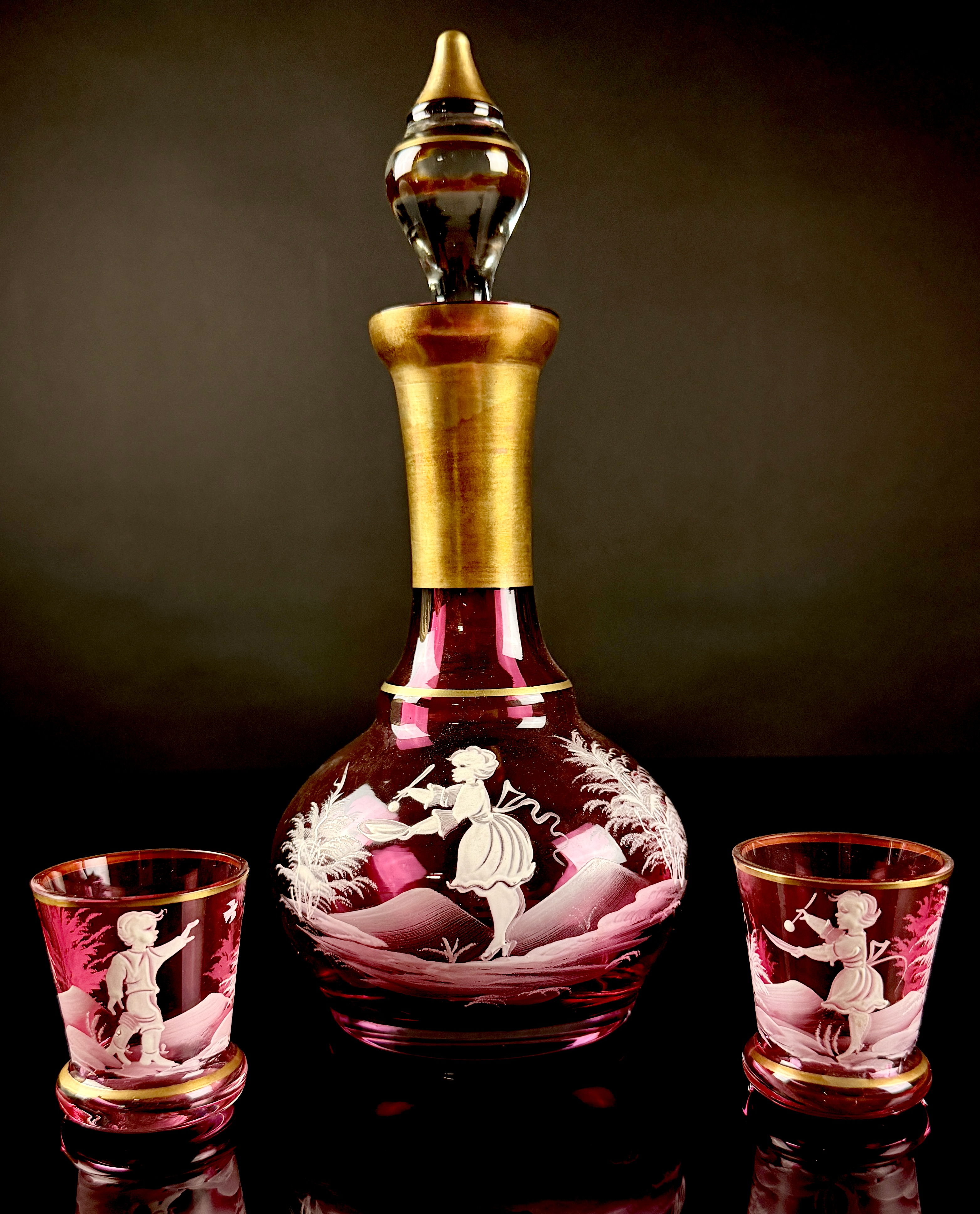 A Trio of Bohemian Mary Gregory Style Cranberry Glass Liqueur Decanter and Cordial Glasses