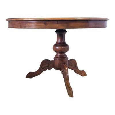 Tavolo tondo in legno di noce retto da balaustro tornito terminante con gambe mosse. 