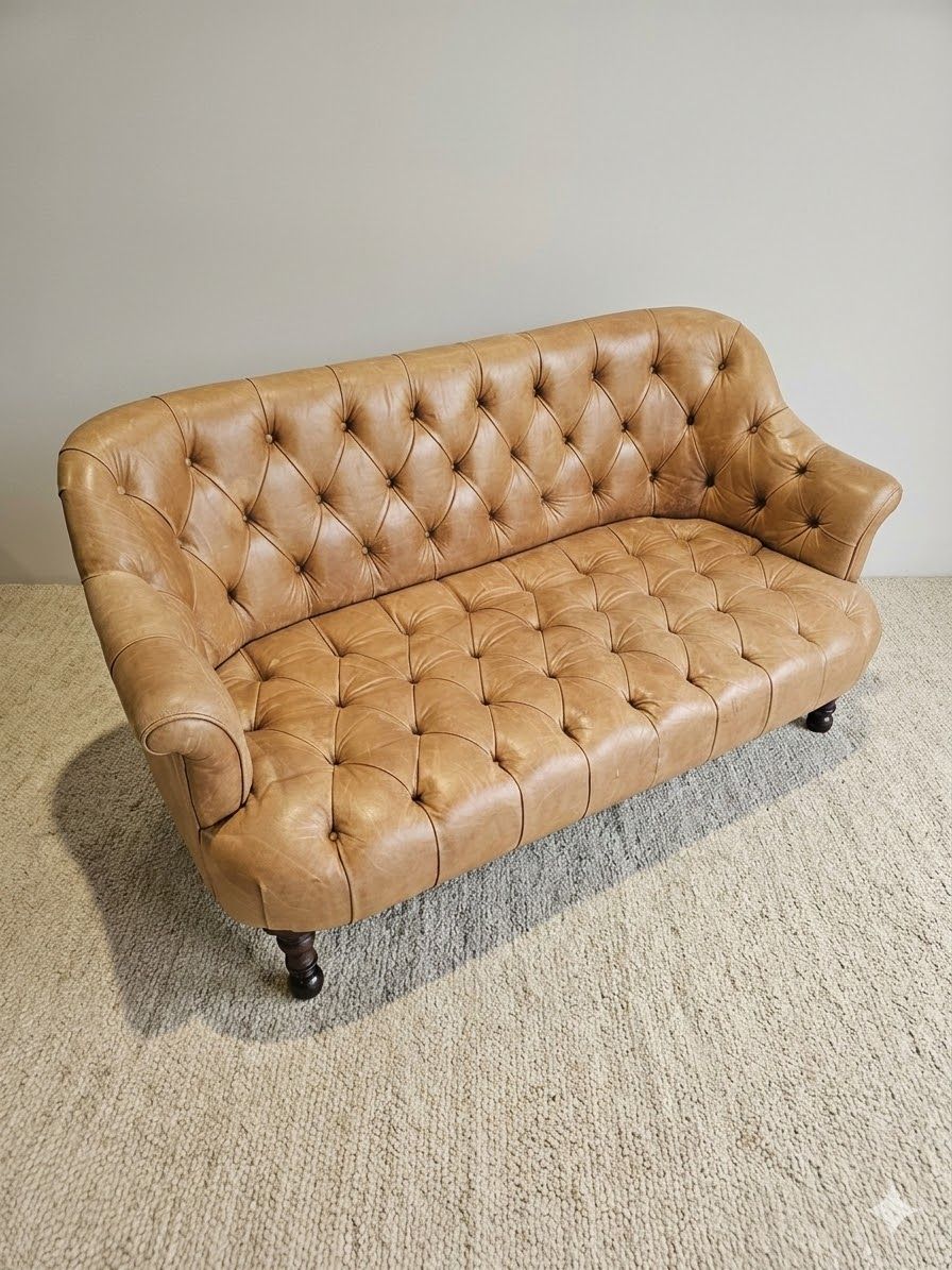 Lot 910: * Chesterfield-style two-seater sofa is upholstered in tan leather and features deep button-tufting