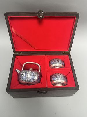A three-piece silver-colored tea set, (possibly silver) comprising a teapot with a gold and 