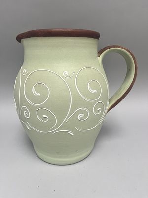 A light green ceramic jug/pitcher with white swirl decoration and a brown rim and handle 