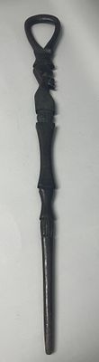 An African carved wood walking stick, featuring an elaborately carved, dark wooden form. The 