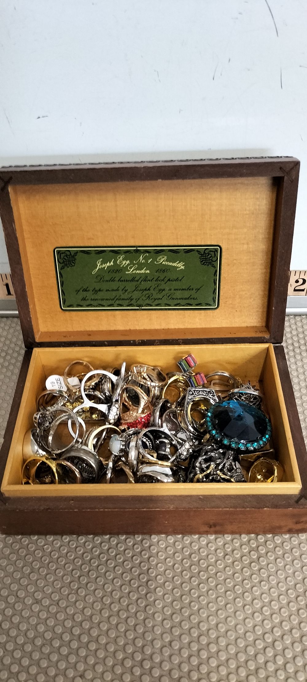 Lot 77 – A Collection of Gold and Silver Costume Rings in a Gun Motif Wooden Presentation Box