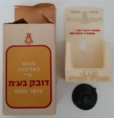 קופסה של דובק חברת סגריות ישראל בתוכה מתקן פלסטיק להנחת קופסת סיגריות. המתקן לצורך לתליה בברכב 