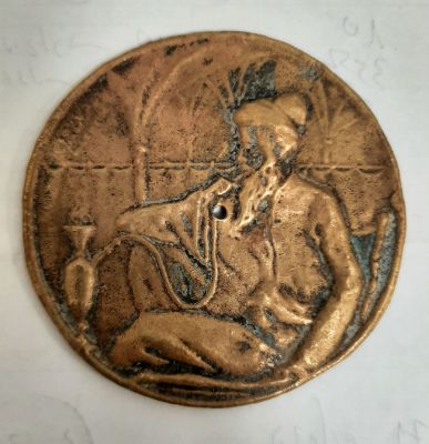 פלאק לוח עם דמות תימני מעשן נרגילה סגנון בצלאל. קוטר 7 ס"מ. חור במרכז כנראה לצורך קיבוע על גבי לוח.