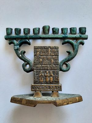 חנוכיה קטנה לא שכיחה עשויה ברונזה עם פטינה ירוקה. כנראה לילדים. מוטיב מתפללם ליג כותל מערבי. 