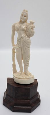 פיגורינה מגולפת בחומר טבעי שן - הב. 
אשה נושאת כד. הפסלון עומד על כן מעץ. 
מידה כולל בסיס : 11 