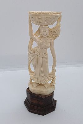 דמות אישה מגולפת בחומר אורגני שן - הב. נושאת סל על הראש ושמלתה מתבדרת ברוח. כנראה נעשה בהודו. 