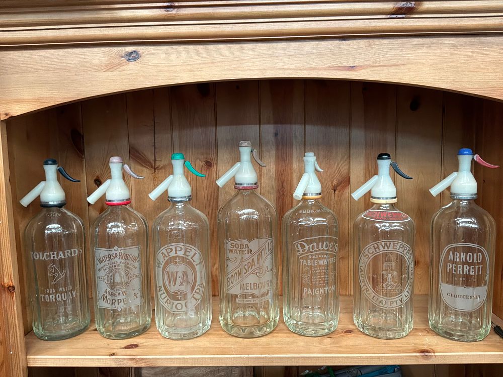 Lot 201: A Collection of Seven Vintage Glass Soda Siphons Including Schweppes and Boon Spa Examples