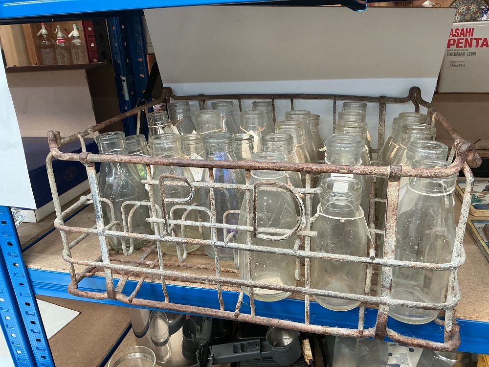 Lot 290: A Collection of Vintage Glass Milk Bottles in a Rusted Wire Delivery Crate
