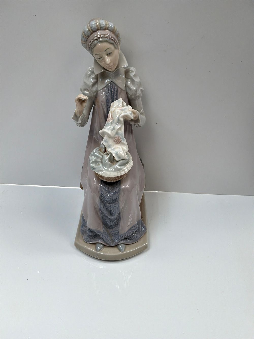 Lot 496: A Spanish Style Glazed Porcelain Figurine of a Seated Woman Sewing