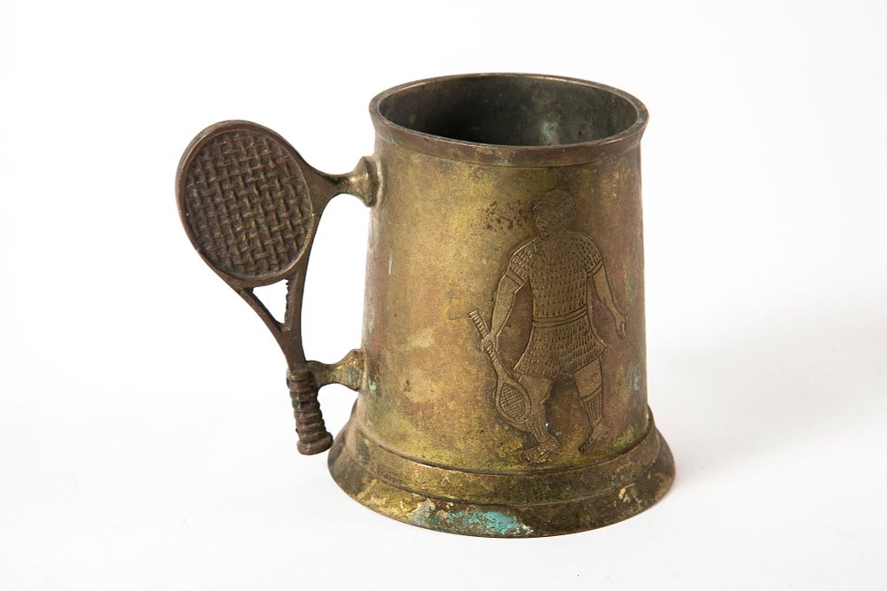 קנקן וינטג' עשוי פליז לחובב טניס . ידית בצורת מחבט טניס ודמות חרוטה של ​​שחקן טניס. 
גובה 12 ס"מ