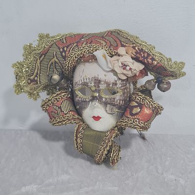 מסכה עשויה מחרס בשילוב עיטורי בד ופעמונים, מאחור לולאה עם סיכה לתליה 
אורך כ 12 ס"מ