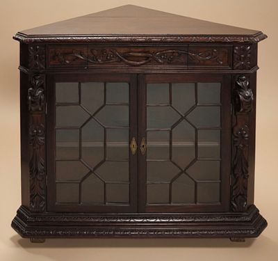 Antique, low, chestnut corner display cabinet with carved details, featuring two small glass 