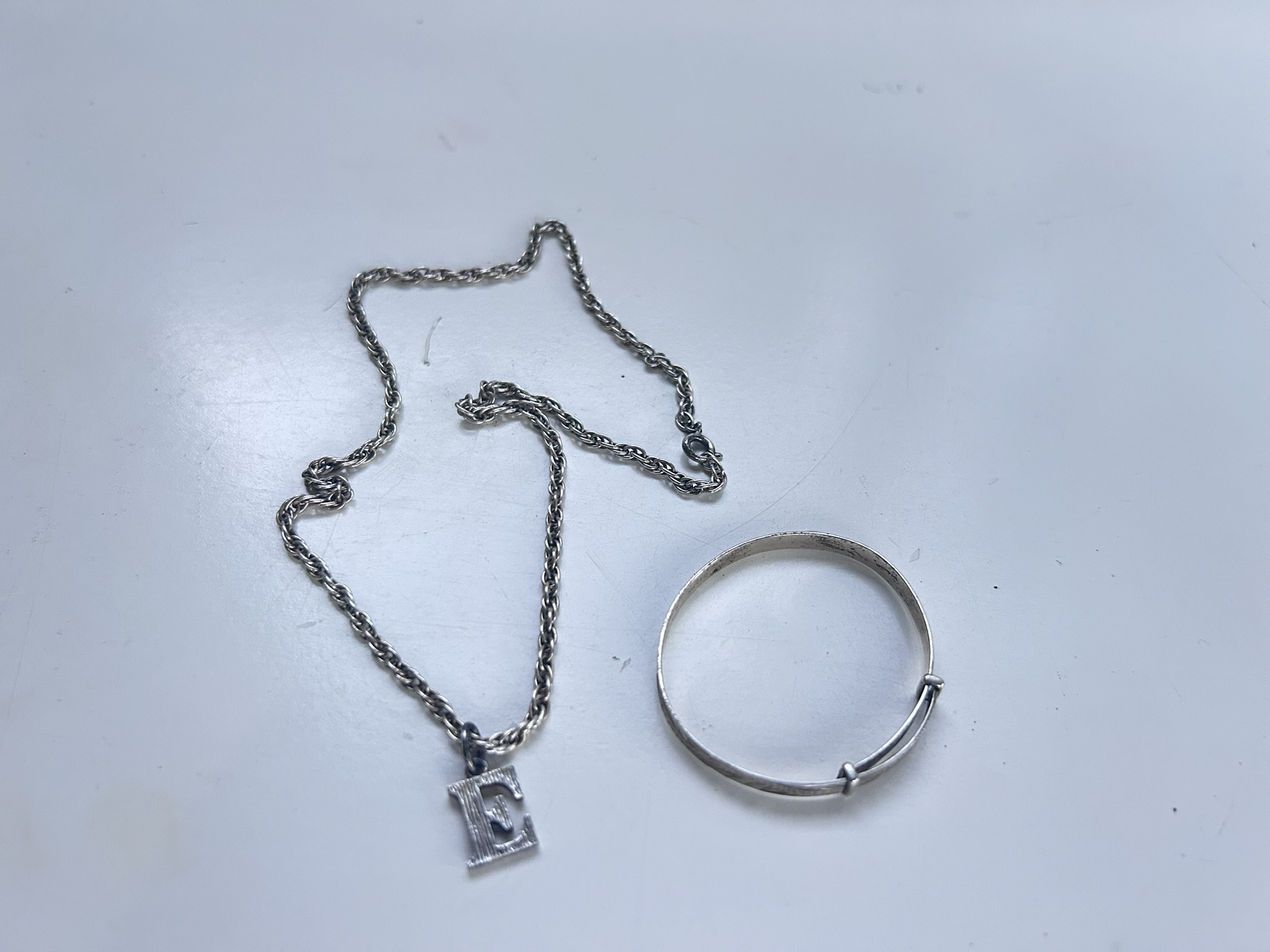 Small silver bangle and a silver chain (both stamped) with a silver name letter "E" unmarked, combined weight circa 28g