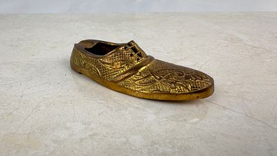 Cenicero individual de bronce con forma de zapato, ornamentado de una finici&oacute;n grabada de 