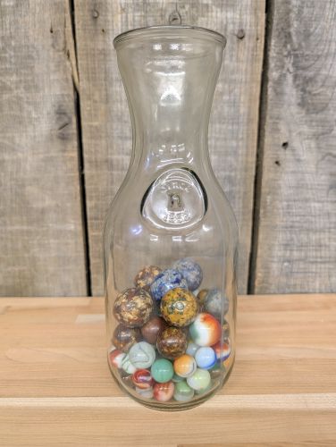 A Collection of Vintage Glass and Clay Marbles in an Embossed Paul Masson Carafe