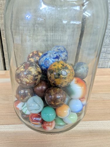 A Collection of Vintage Glass and Clay Marbles in an Embossed Paul Masson Carafe