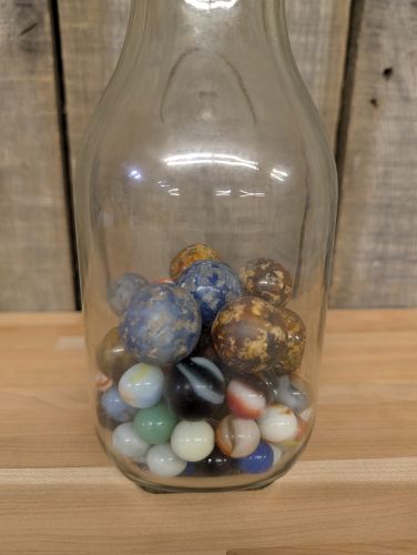 A Collection of Vintage Glass and Clay Marbles in an Embossed Paul Masson Carafe