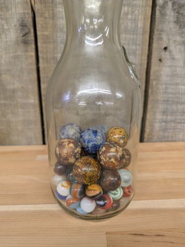 A Collection of Vintage Glass and Clay Marbles in an Embossed Paul Masson Carafe