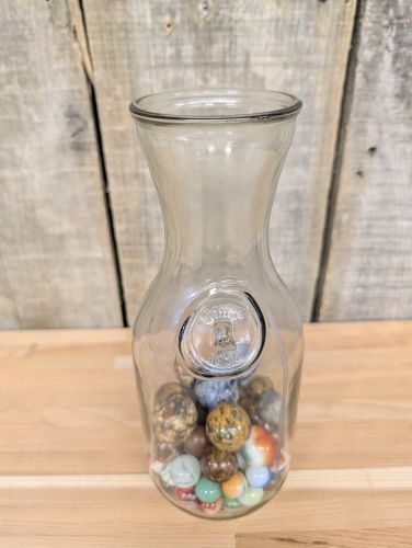 A Collection of Vintage Glass and Clay Marbles in an Embossed Paul Masson Carafe