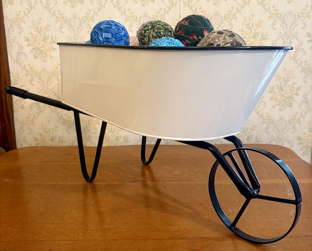 Lot 261: Large Decorative White Metal Wheelbarrow with Assortment of Fabric Rag Balls