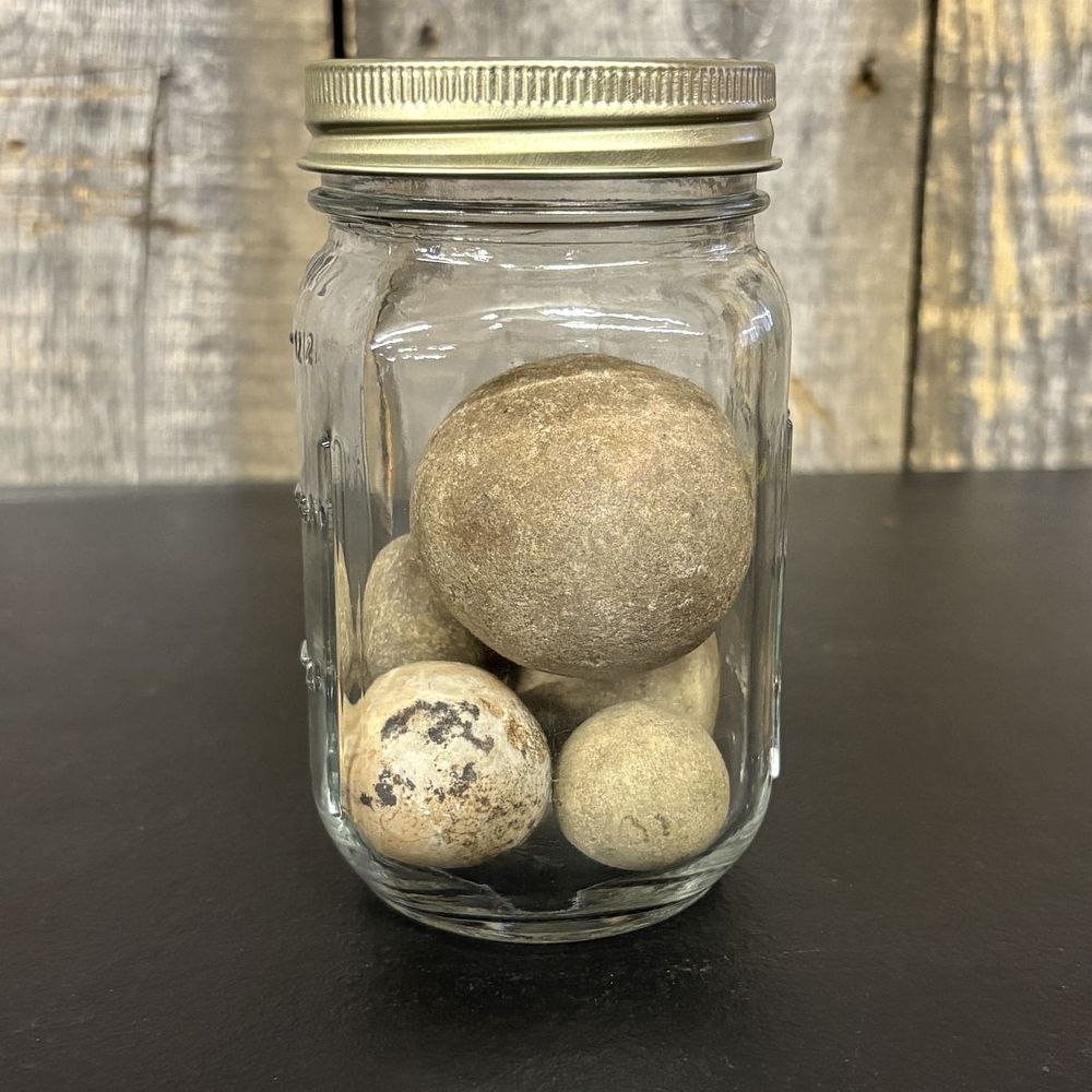 Lot 437: A Group of Five Spherical Stone Game Balls or Projectiles in a Glass Jar