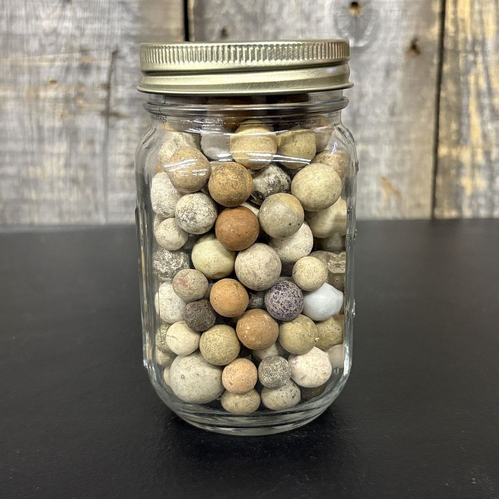 Lot 665: A Collection of Antique Clay Marbles in a Graduated Glass Jar