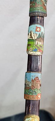 פריט אספנות מקל הליכה שוויצרי מעץ מעוטר ב 8 לוחיות מזכרת ממתכת ואמייל המציגות נופים ושמות האתרים. 