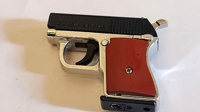 מצית בצורת אקדח מיניאטורי, הגוף עשוי מתכת בגוון ניקל, ידיות פלסטיק. . חתום במספרים סידוריים - 