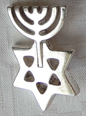 סיכה בצורת מגן דוד ומנורה מצופה כסף בסגנון יעקב אגם. 
גודל: 4.2X2.7 ס"מ. 
משקל: 28 גרם.