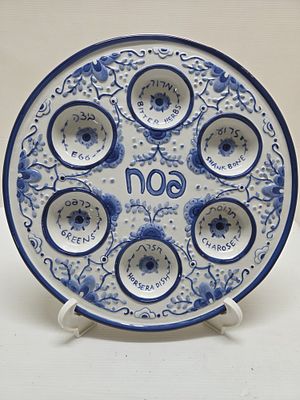 צלחת פסח. צלחת סדר פסח בכחול לבן, מקושטת בפרחים עם שקעים עליהם מצוינות הברכות באנגלית ועברית. 