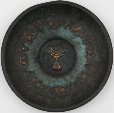 צלחת נחושת לתלייה, נושאת תבליט של המנורה, גפנים ופירות ארצנו. פטינה נהדרת. לא חתומה. כיפוף בשפה 